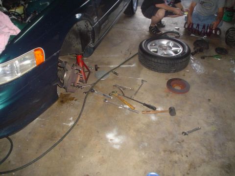1993 Ford Taurus - Car repair in progress: front wheel assembly removed, with tools and parts scattered around.