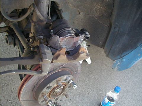 1993 Ford Probe - Close-up view of a vehicle's brake caliper and rotor, with a bottle of water visible on the asphalt.
