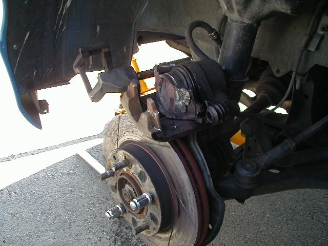 Close-up of a car's front brake caliper and rotor assembly, showing wear