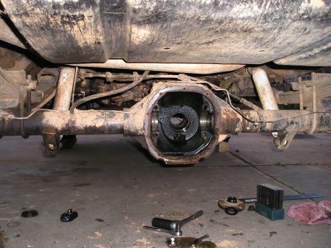 1996 Ford Bronco - Underside view of a vehicle's rear differential removed for service, with tools laid out on the concrete floor.