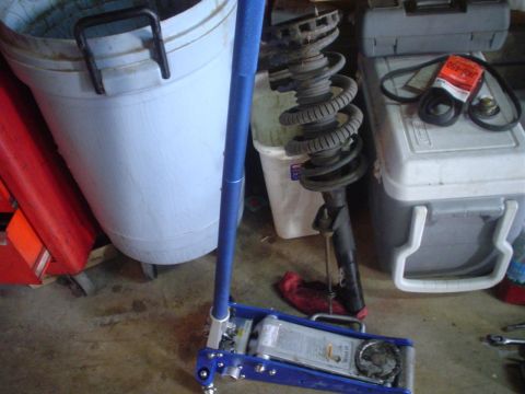 1993 Ford Taurus - A car strut assembly and a hydraulic jack are shown next to a cooler and a large bin.