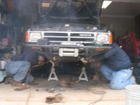 1986 Ford F-150 - Two mechanics work on the front bumper of a Toyota truck in a garage.