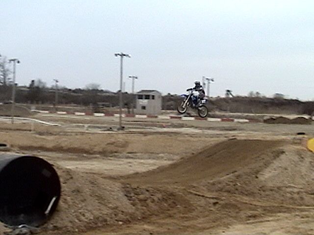 Motocross rider jumping a dirt bike over a berm at an outdoor dirt track