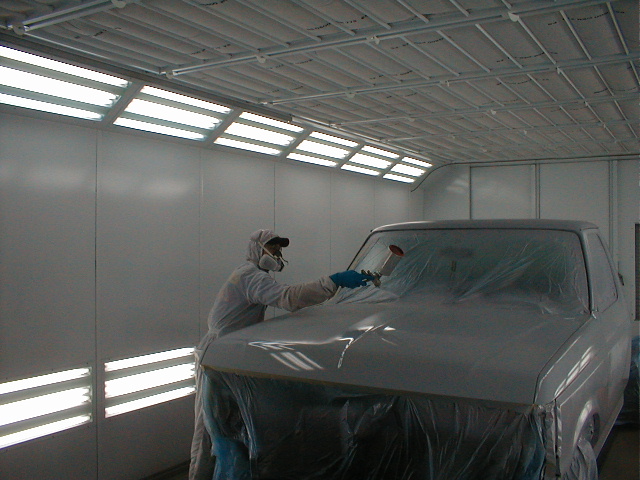 Painter in protective suit spraying gray primer on masked truck hood inside a paint booth