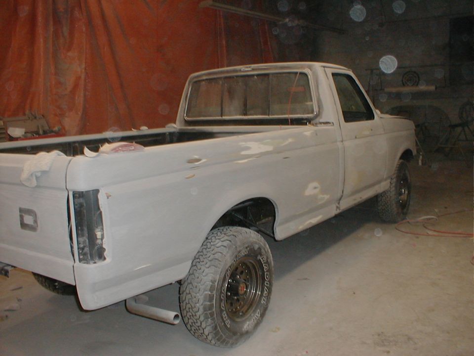 Ford F-150 pickup in gray primer with all-terrain tires, rear three-quarter view in a garage