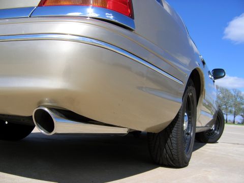 2000 Ford Crown Victoria - Close-up of a car's rear quarter panel, highlighting the chrome trim and exhaust pipe under a blue sky.