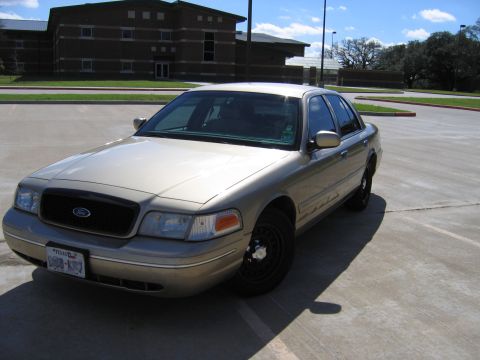 2000 Ford Crown Victoria - A gold Ford Crown Victoria is parked in a lot with a building in the background.