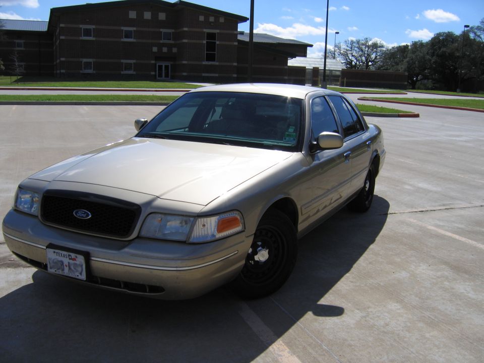 Gold Ford Crown Victoria with black grille and steel wheels, parked on a concrete lot