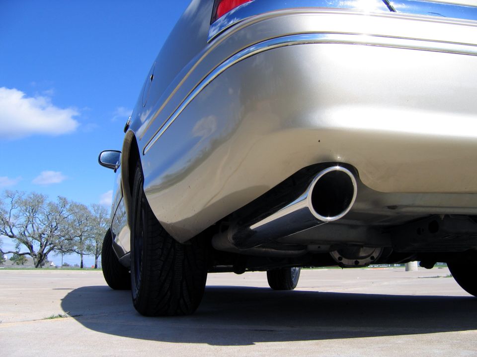 Low-angle view of a polished exhaust tip under a gold sedan's rear bumper