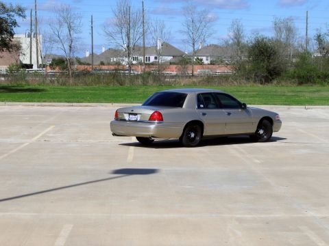 2000 Ford Crown Victoria - A tan 2000 Ford Crown Victoria sedan is parked in an empty lot under a partly cloudy sky.