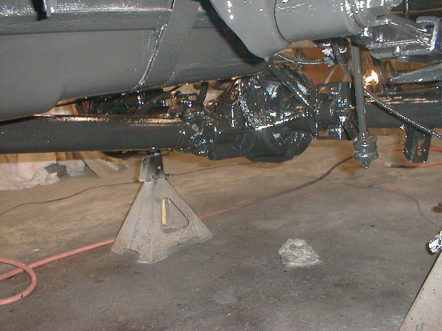 Underside of a vehicle on jack stands, showing the rear axle and suspension parts that have been painted black