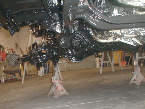 1991 Ford F-150 - The underside of a vehicle is shown on jack stands, covered in black paint, with some foil insulation.