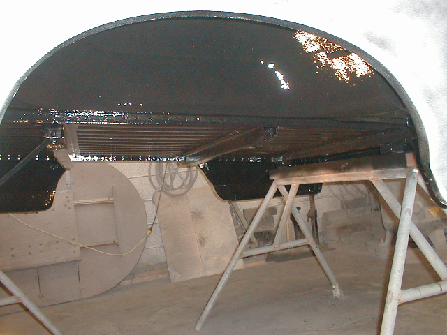 Underbody of a vehicle on jack stands, showing black coating and some structural components