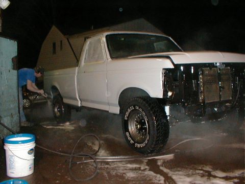 1991 Ford F-150 - A person washes a white pickup truck that is missing its front grille and bumper.