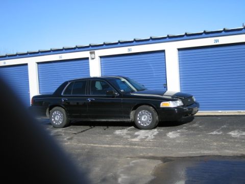 1991 Ford LTD Crown Victoria - Side view of a black 1991 Ford Crown Victoria LTD parked in front of blue storage unit doors.