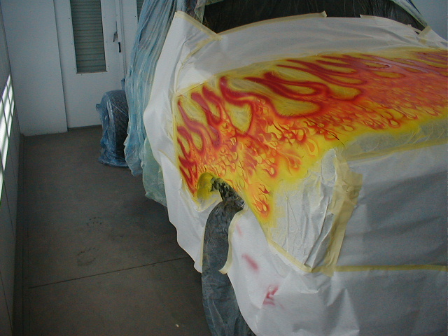 Side of a masked vehicle with airbrushed red and yellow flames, painter in coveralls working