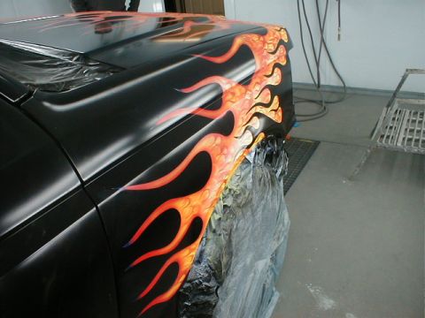 1991 Ford F-150 - A car fender is being painted with custom flame graphics in a workshop.