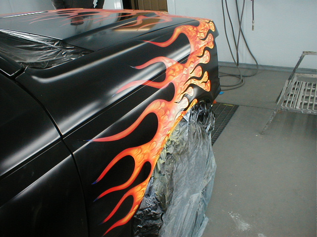 black car fender with orange and red flames painted on it, being worked on in a garage