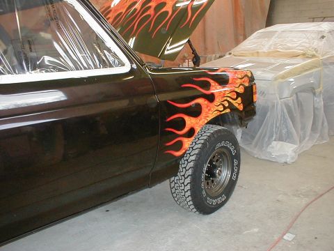 1991 Ford F-150 - A truck with custom flame paint is being worked on, with another vehicle covered in plastic in the background.