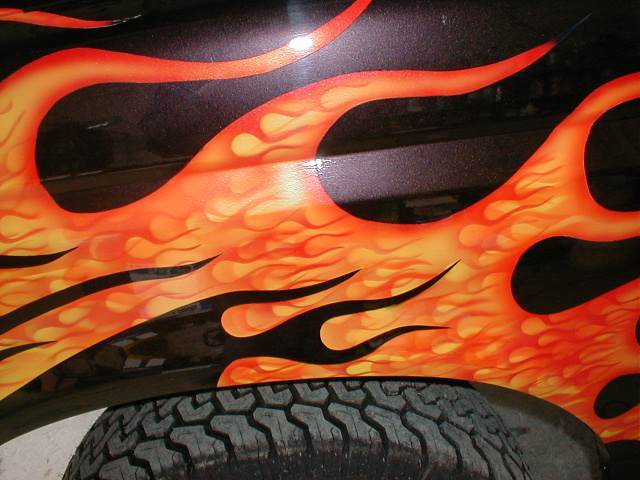 Close-up of orange and yellow flames painted on a black vehicle fender above a tire