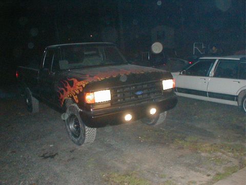 1991 Ford F-150 - A black 1991 Ford F-150 pickup truck is parked outdoors at night, custom flame paintwork on the hood and fenders.