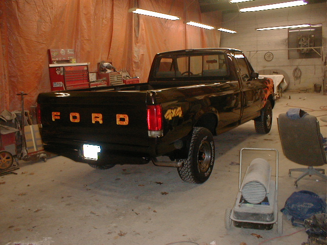 1991 Ford F-150 pickup truck, black with orange flames on the fender, parked in a garage