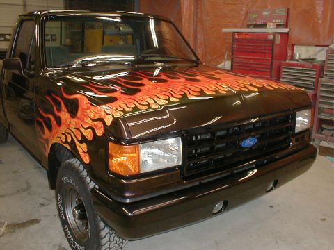 1991 Ford F-150 - This pickup truck features a custom flame paint job on its dark brown exterior, with the Ford logo visible on the grille.
