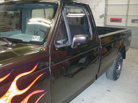 1991 Ford F-150 - This pickup truck features custom flame graphics on its side, with a sticker visible on the driver's side window.