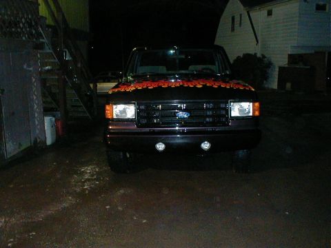 1991 Ford F-150 - This 1991 Ford F-150 features custom orange flame graphics on its hood, viewed from the front at night.