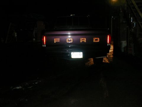 1991 Ford F-150 - The rear of a 1991 Ford F-150 pickup truck is visible in the dark, showing its tailgate with chrome lettering.