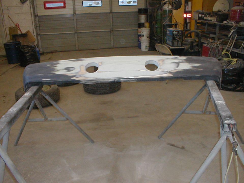Primered fiberglass bumper or panel with two round cutouts resting on sawhorses in a garage