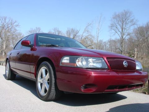 1998 Ford Crown Victoria - A maroon/dark red four-door sedan photographed from the front three-quarter angle, showing a waterfall-style chrome grille with a badge, cl…