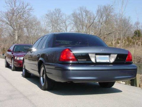 1998 Ford Crown Victoria - Rear three-quarter view of a dark blue-gray Ford Crown Victoria sedan parked on a paved road, with a maroon sedan of similar body style par…