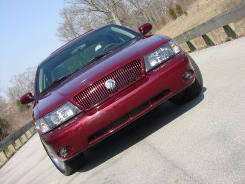 1998 Ford Crown Victoria - Low front view of a dark-red full-size sedan fitted with a blacked-out slotted grille bearing a Mercury emblem, with clear headlamps and bu…