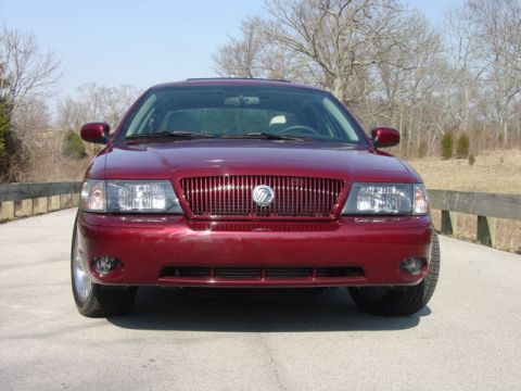 1998 Ford Crown Victoria - Head-on front view of a dark cherry-red Mercury full-size sedan with a body-color vertical-bar grille, Mercury emblem and clear headlights,…