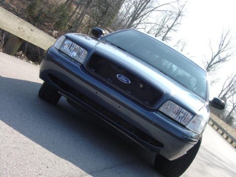 1998 Ford Crown Victoria - A dark blue Ford Crown Victoria sedan shot from a low tilted angle at the front, filling the frame with the mesh grille, Ford oval badge an…