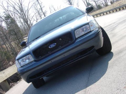 1998 Ford Crown Victoria - Low, slanted front three-quarter view of a steel-blue Ford Crown Victoria with a black crosshatch grille and Ford oval, shot from near pave…