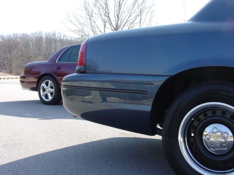 1998 Ford Crown Victoria - Close low angle along the rear quarter and bumper of a slate-gray Ford Crown Victoria, showing its black steel wheel dressed with a chrome…