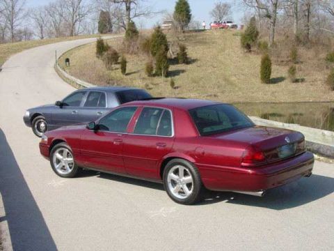 1998 Ford Crown Victoria - Elevated rear three-quarter view of a dark red Mercury Marauder-style full-size sedan with five-spoke machined alloys and dual exhaust tips…