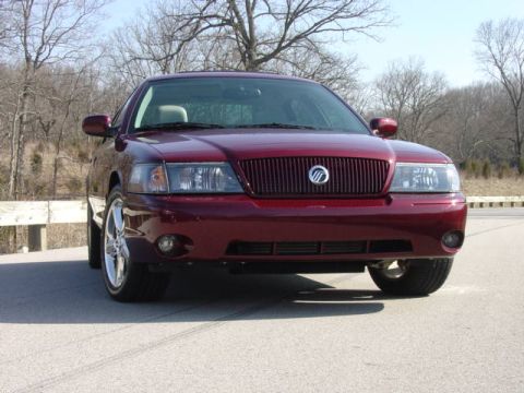 1998 Ford Crown Victoria - Low front view of a dark toreador-red Mercury full-size sedan with a vertical-slat waterfall grille and Mercury emblem, clear-lens headlamp…