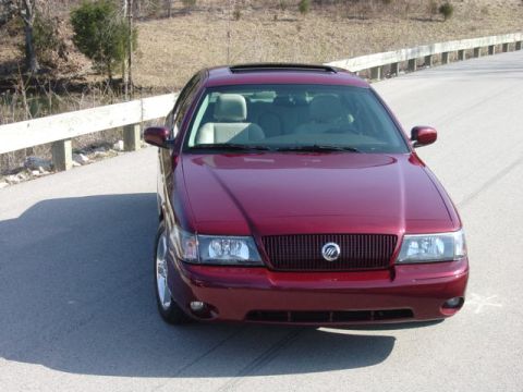 1998 Ford Crown Victoria - A maroon Mercury sedan photographed head-on on a bridge, with a sunroof, a waterfall-style chrome grille bearing the Mercury emblem, and a…