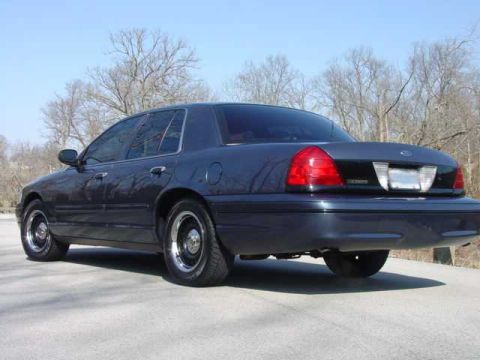 1998 Ford Crown Victoria - A dark blue/gray Ford Crown Victoria full-size sedan photographed from the rear driver's side (3q-rear angle), showing the taillights, Ford…