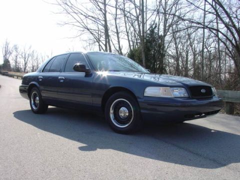1998 Ford Crown Victoria - Front three-quarter view of a dark blue Ford Crown Victoria police-package sedan parked on a bridge, wearing black steel wheels with chrome…