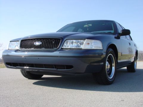 1998 Ford Crown Victoria - Low-angle front three-quarter view of a dark blue Ford Crown Victoria with a black honeycomb grille and clear headlights, wearing black pol…