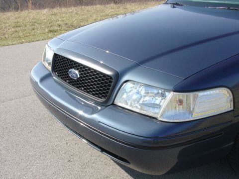 1998 Ford Crown Victoria - Close-up of the front corner of a slate-blue Ford Crown Victoria showing a black honeycomb-mesh grille with a Ford oval emblem and a clear…