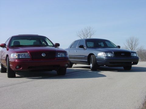 1998 Ford Crown Victoria - maroon Mercury sedan and a gray Ford Crown Victoria parked nose to nose in an empty lot.