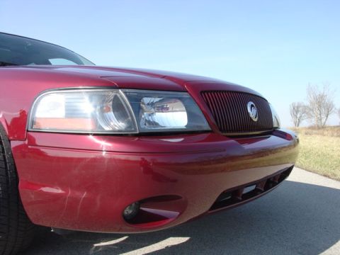 1998 Ford Crown Victoria - Low-angle close-up of the front corner of a dark red sedan wearing a Mercury Marauder-style front end, with a vertical-slat grille, Mercury…