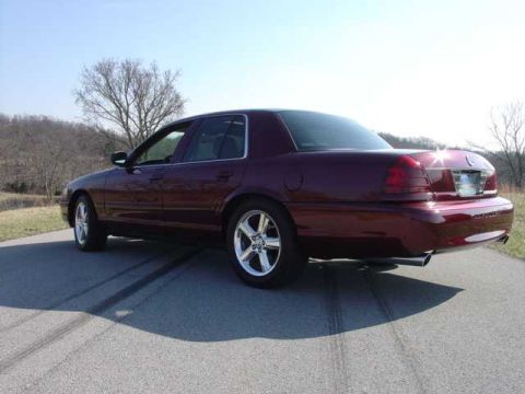 1998 Ford Crown Victoria - Rear three-quarter view of a dark burgundy Mercury Marauder-style full-size sedan parked on a rural asphalt road, with chrome polished-allo…