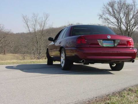1998 Ford Crown Victoria - dark red Mercury Marauder four-door sedan is photographed from the rear three-quarter angle on a quiet country road.
