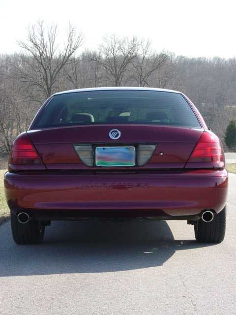 1998 Ford Crown Victoria - Straight-on rear view of a dark burgundy Panther-platform Ford sedan wearing a Mercury-badged rear applique panel between smoked taillights…